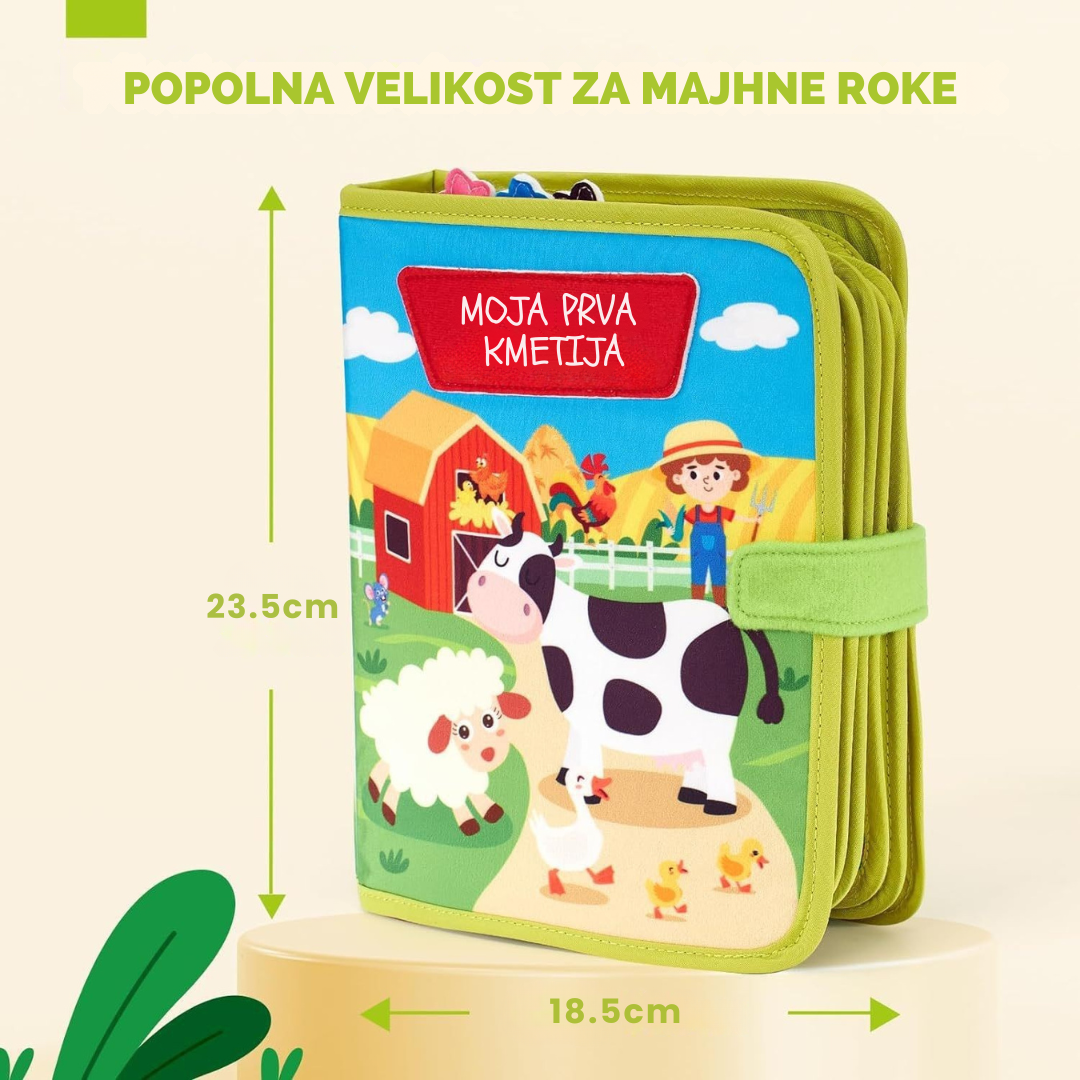 Grafični prikaz mehke interaktivne knjige z naslovom "Moja prva kmetija", ki prikazuje njene dimenzije: 23.5 cm v višino in 18.5 cm v širino. Besedilo na sliki poudarja, da je to popolna velikost za majhne roke.